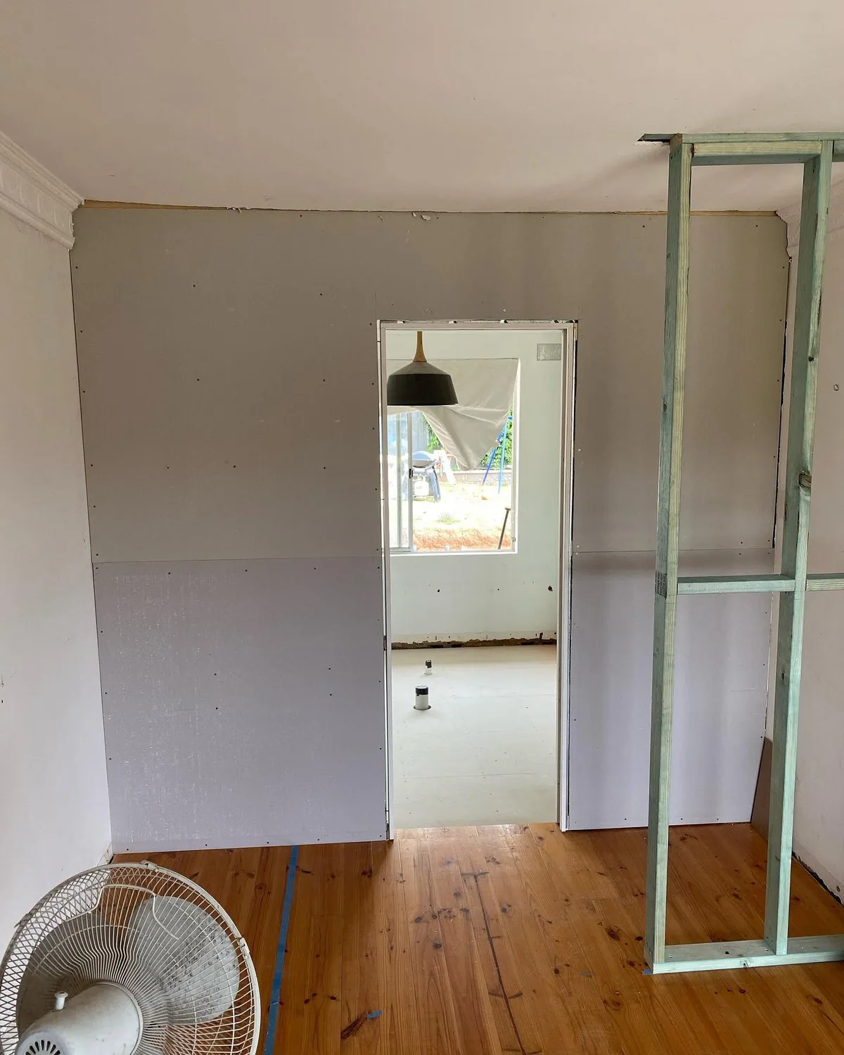 Bathroom in the early stage of a renovation, with new wall sheeting, bare timber floorboards and light steel framing for a new wall