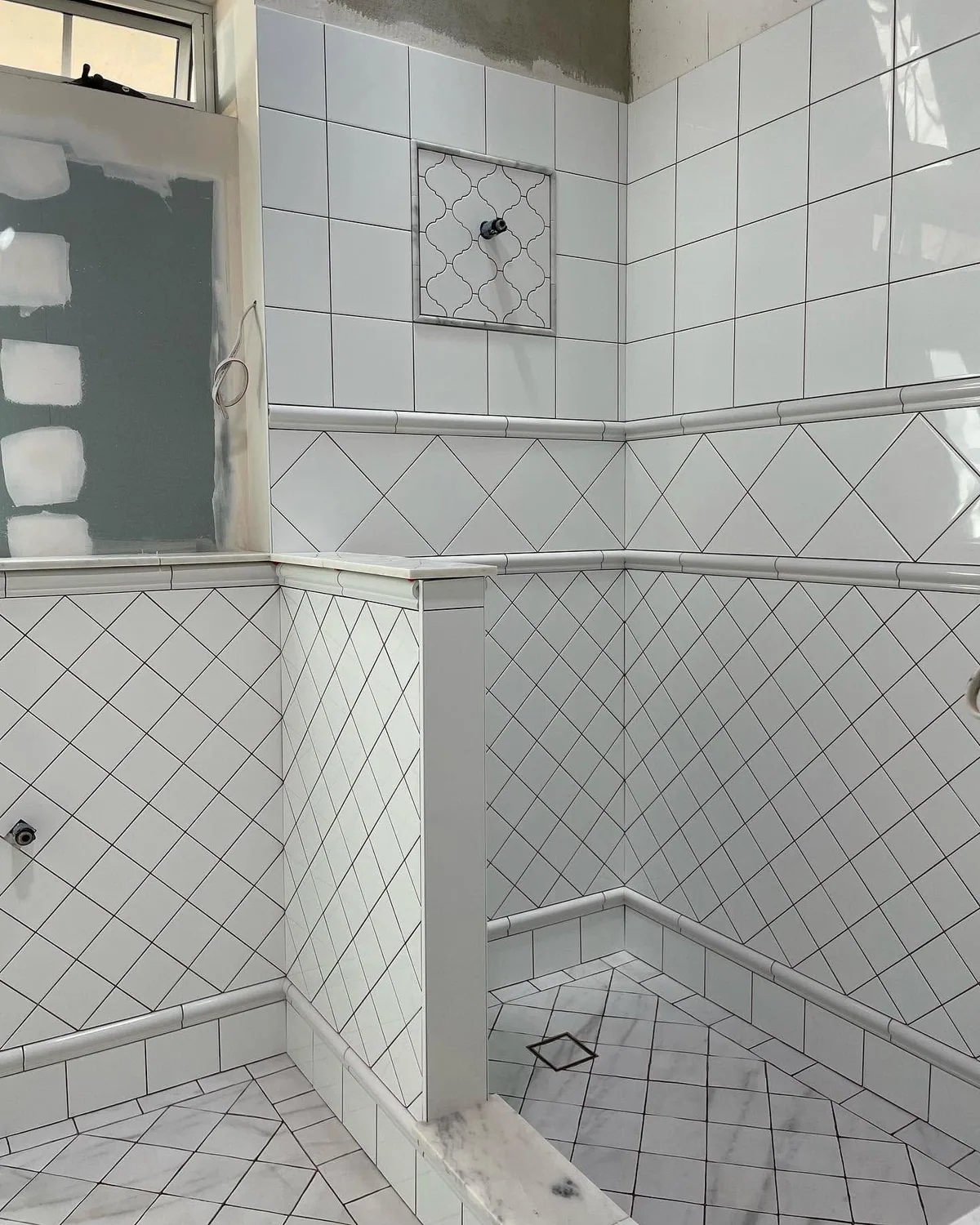 Diamond-set white wall tiles and matching floor tiles being laid in a shower area during a bathroom renovation