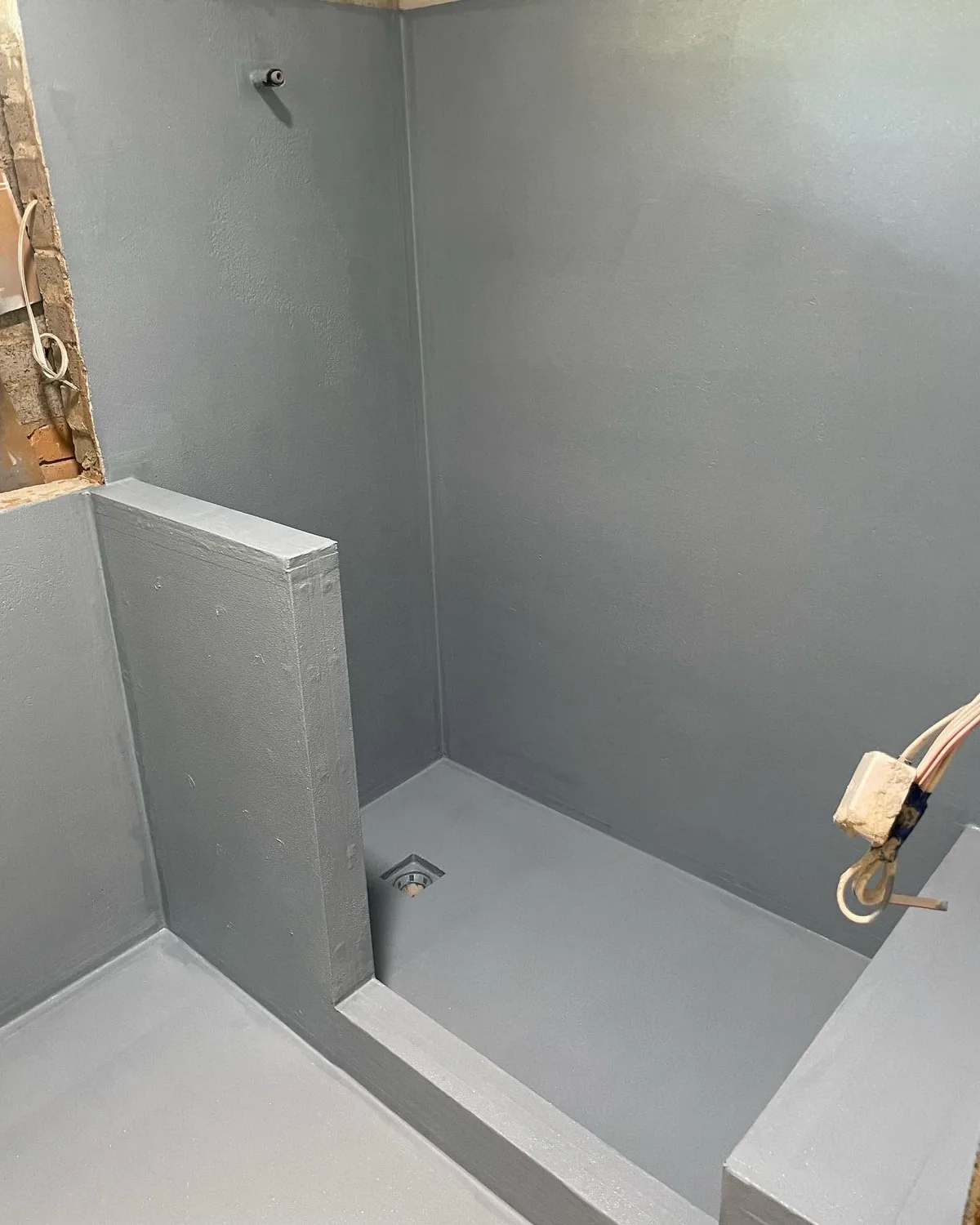Shower recess stripped back to the substrate with a fresh grey waterproofing membrane over the floor, hob and walls before re-tiling