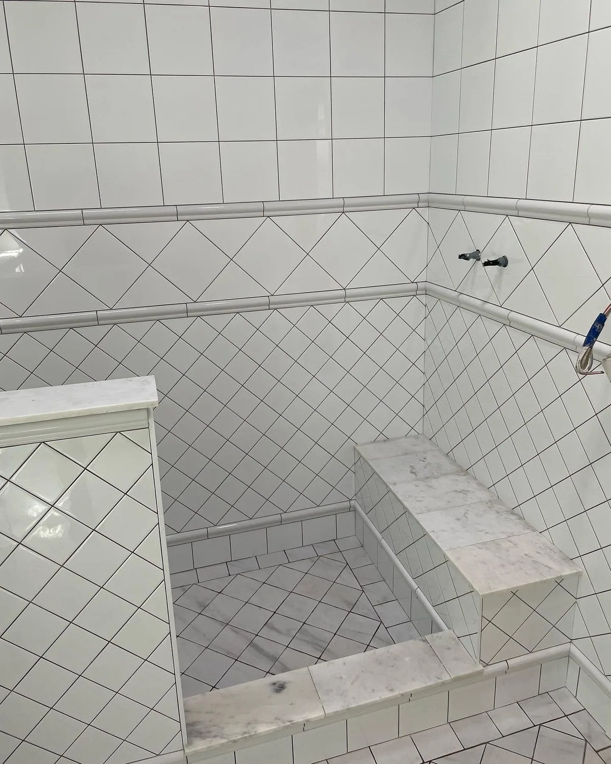 Diamond-set white wall tiles, a tiled shower floor and a marble-look shower seat in a renovated bathroom