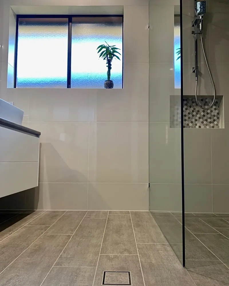 Finished walk-in shower with a frameless glass screen, grey floor tiles falling to a square floor waste and a mosaic niche
