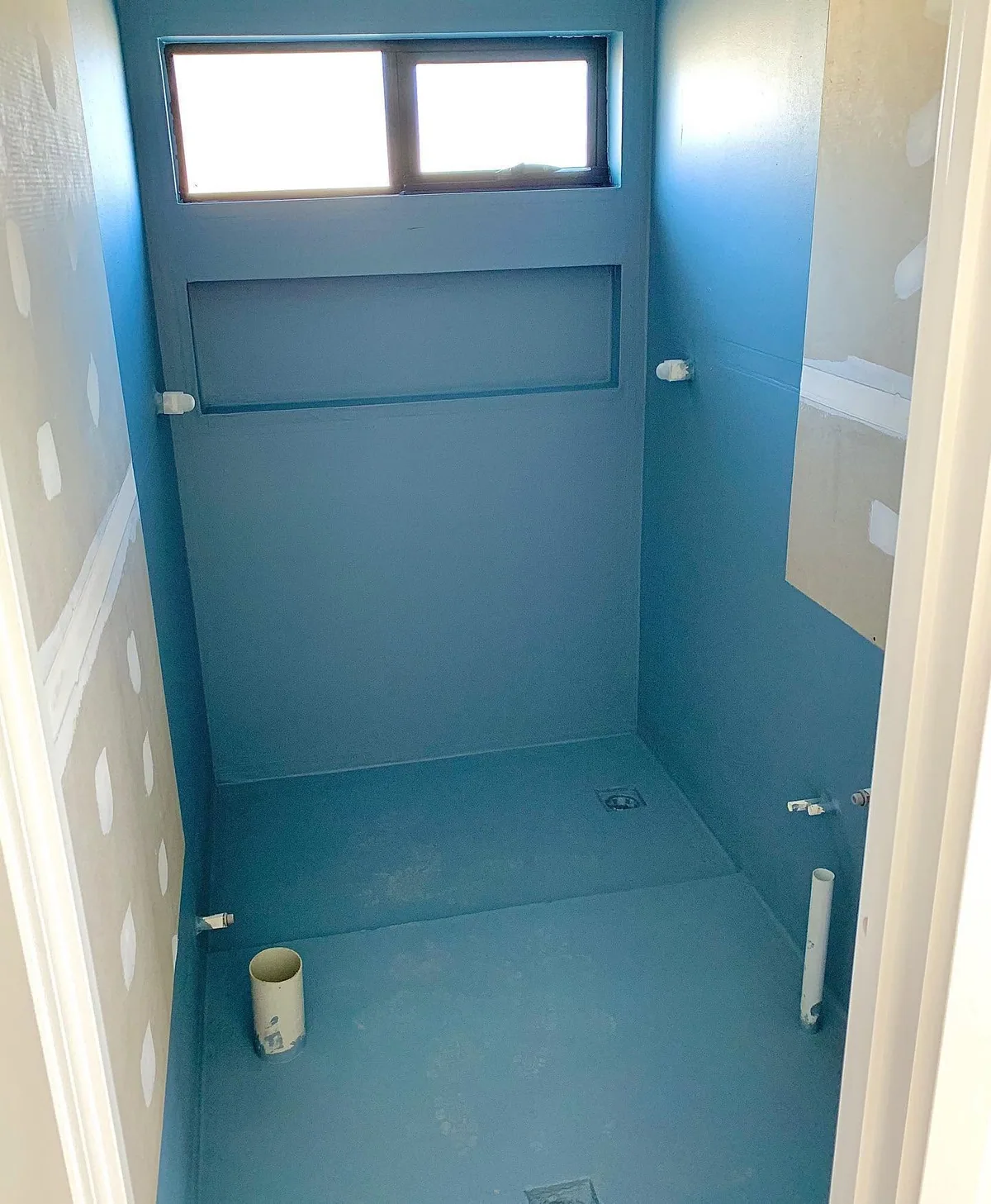 Narrow shower recess coated in blue waterproofing membrane on the floor and walls, with a wall niche and capped tap penetrations